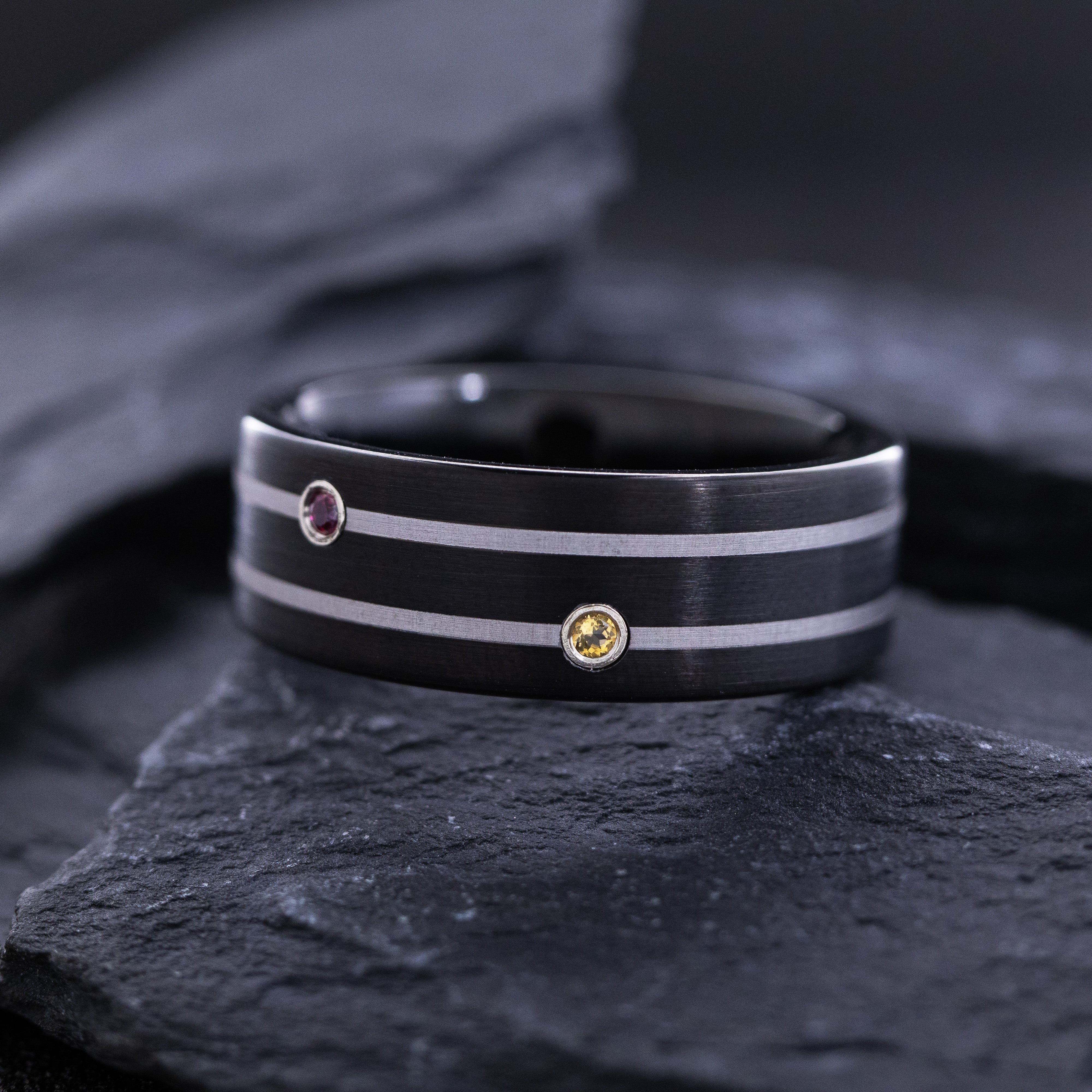 Black ring with embedded gemstones on a dark stone surface