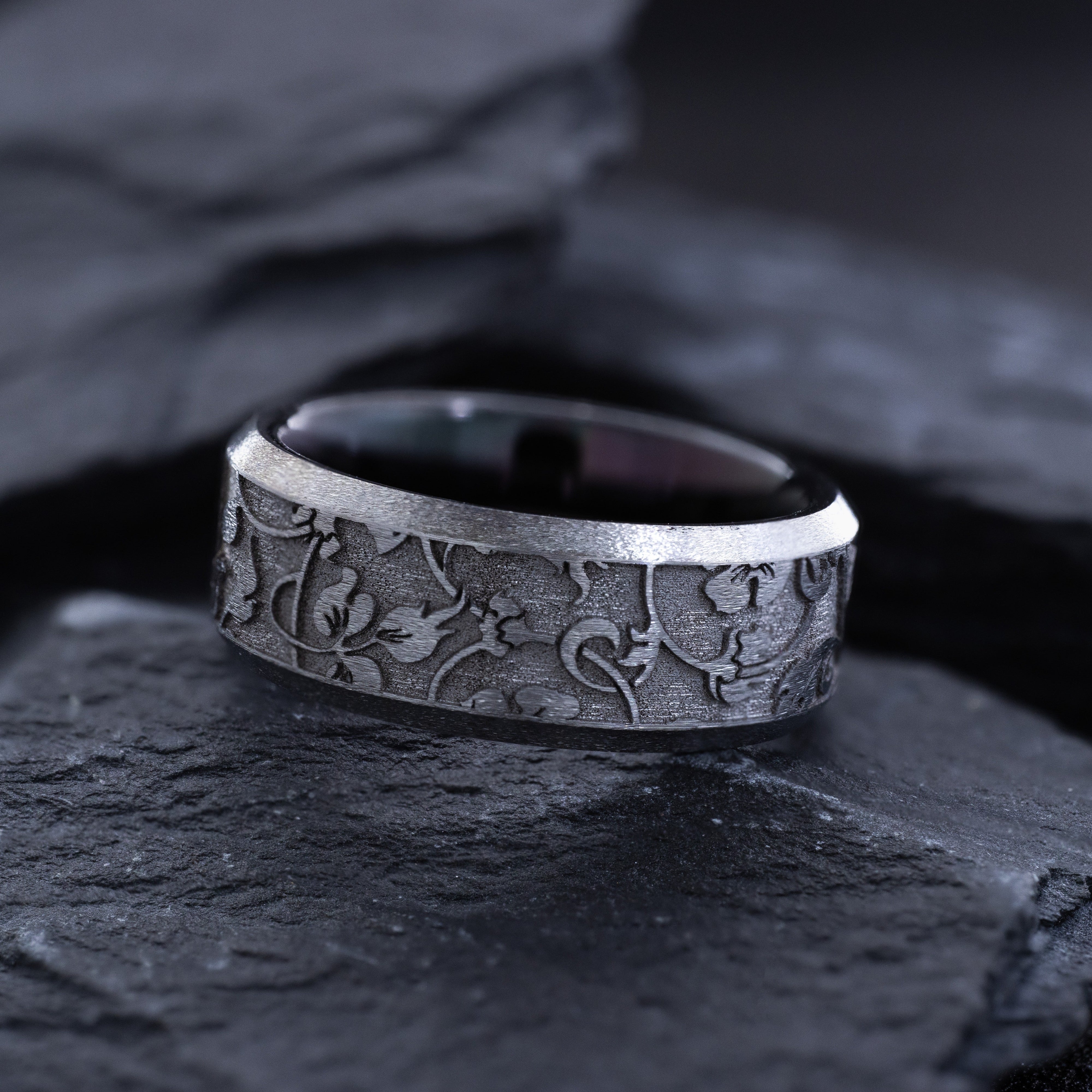 Silver ring with intricate designs on a dark stone surface