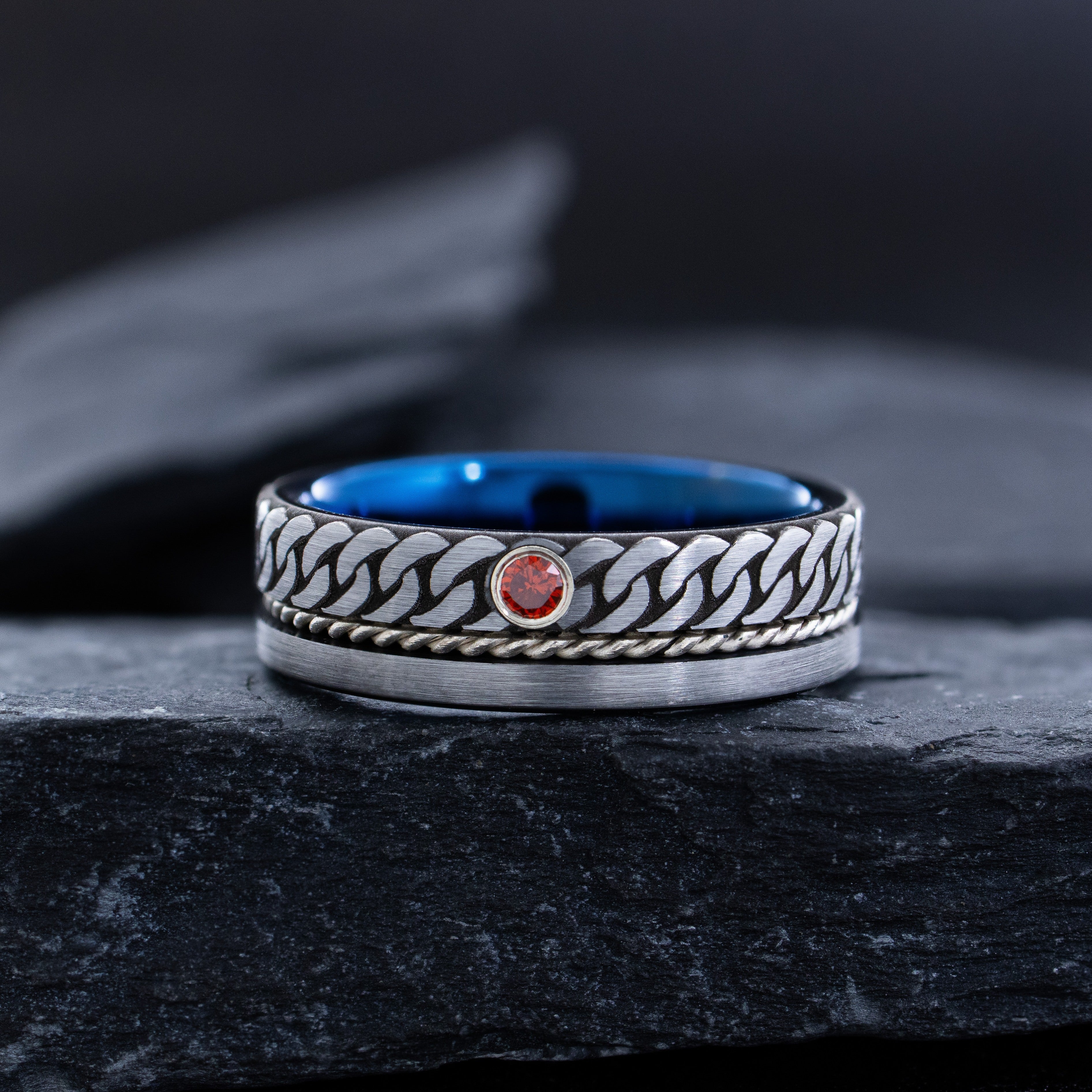 Silver ring with blue interior and red gemstone on a dark stone surface
