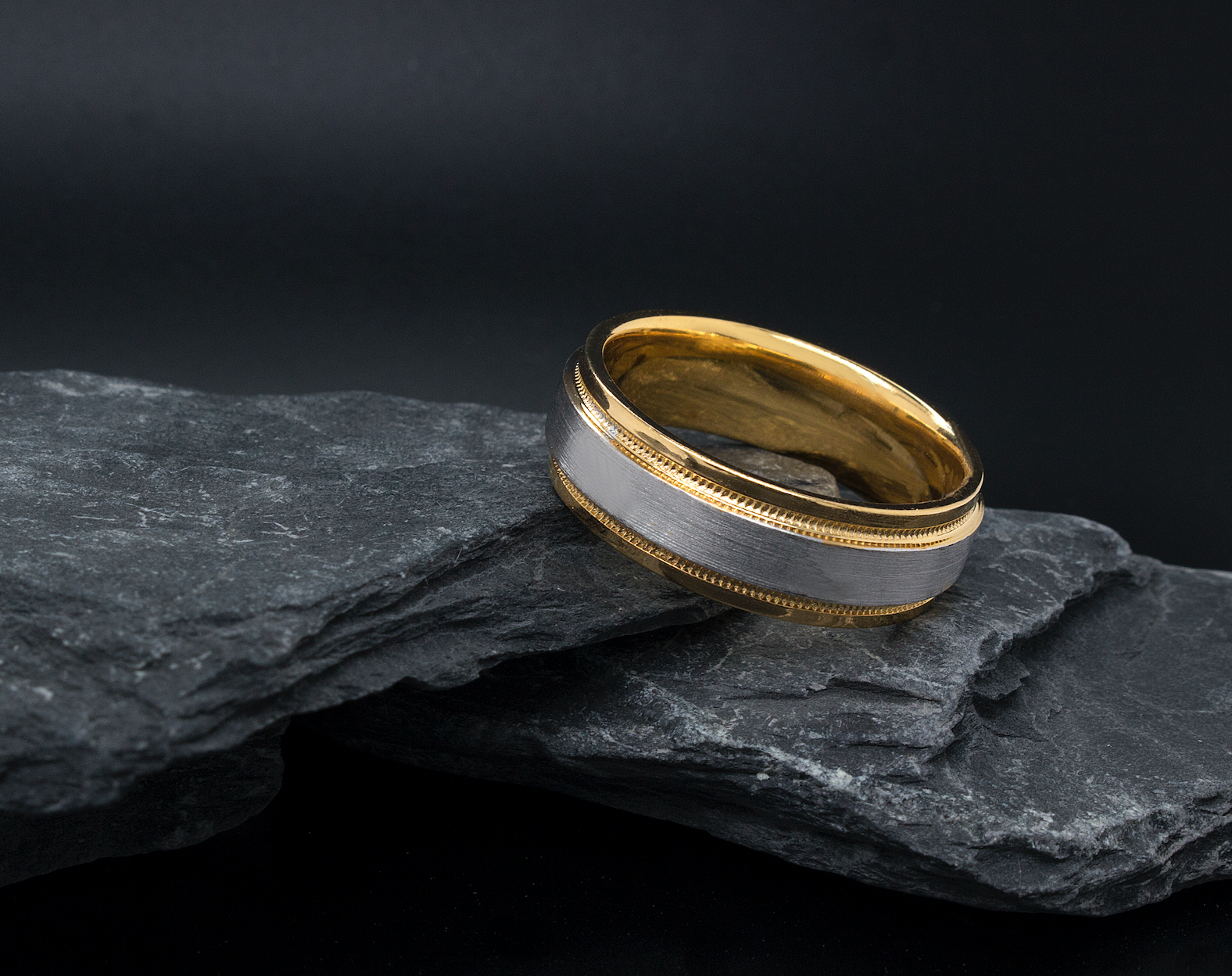 ring, ring on black background, mens rings, womens ring, unisex ring, two toned ring, yellow gold and white gold ring, brushed center, polished edges and interior, migrain engraving, stepped edges, wedding band, mens wedding band, womens wedding band, minimalist ring